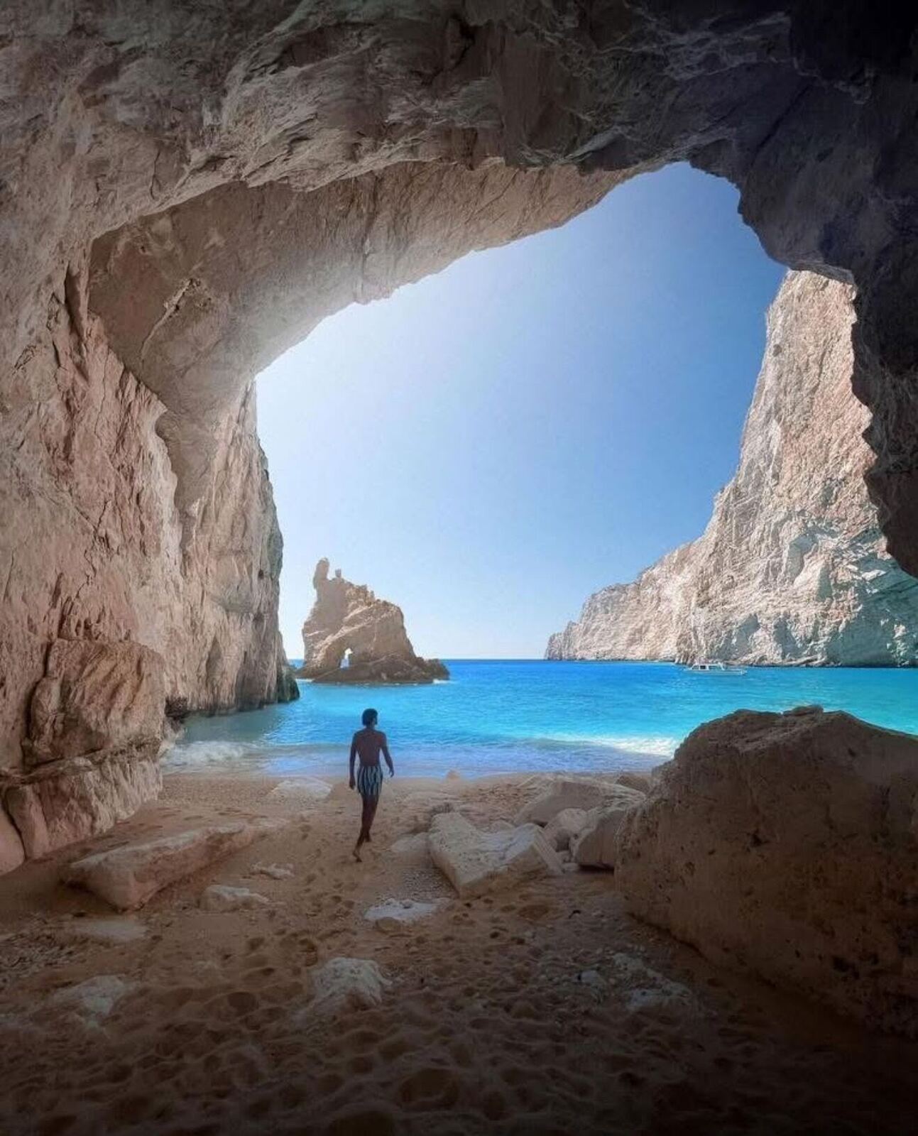 Silhouette of a person walking inside Eros Cave with the heart-shaped opening framing the turquoise sea