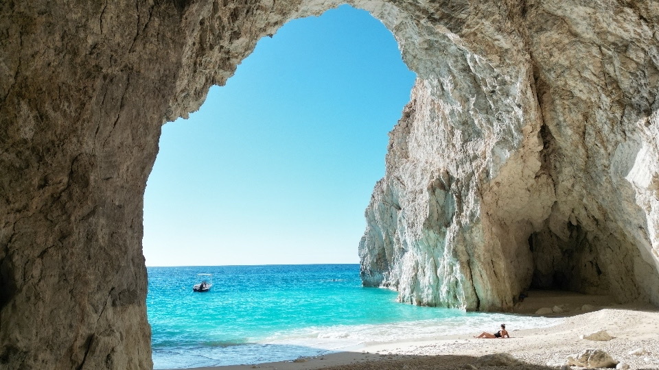 Wide view from inside Eros Cave looking out through the arch to the sea and a distant boat