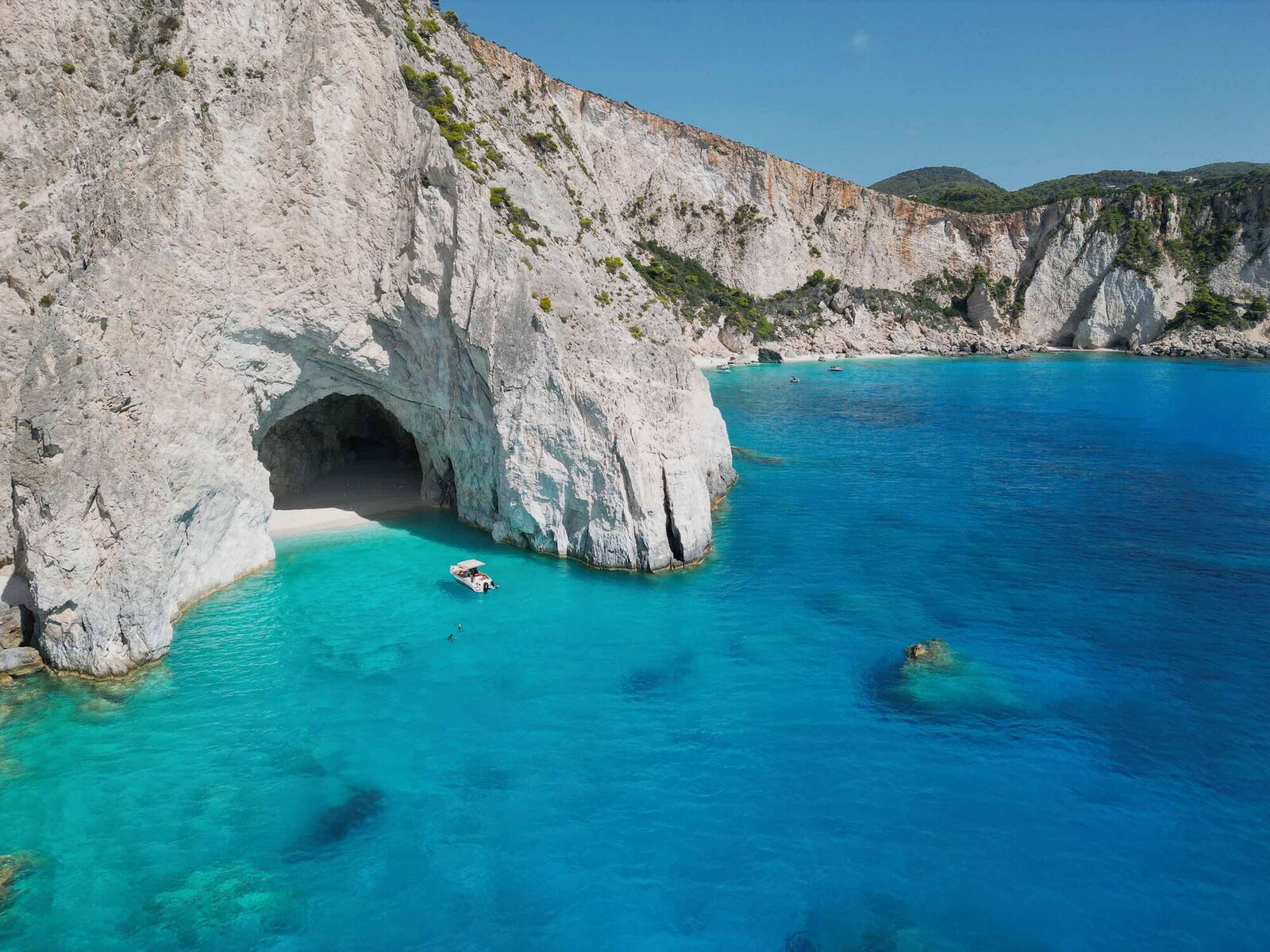 Aerial view of Eros Cave entrance with a boat anchored in the crystal-clear turquoise water