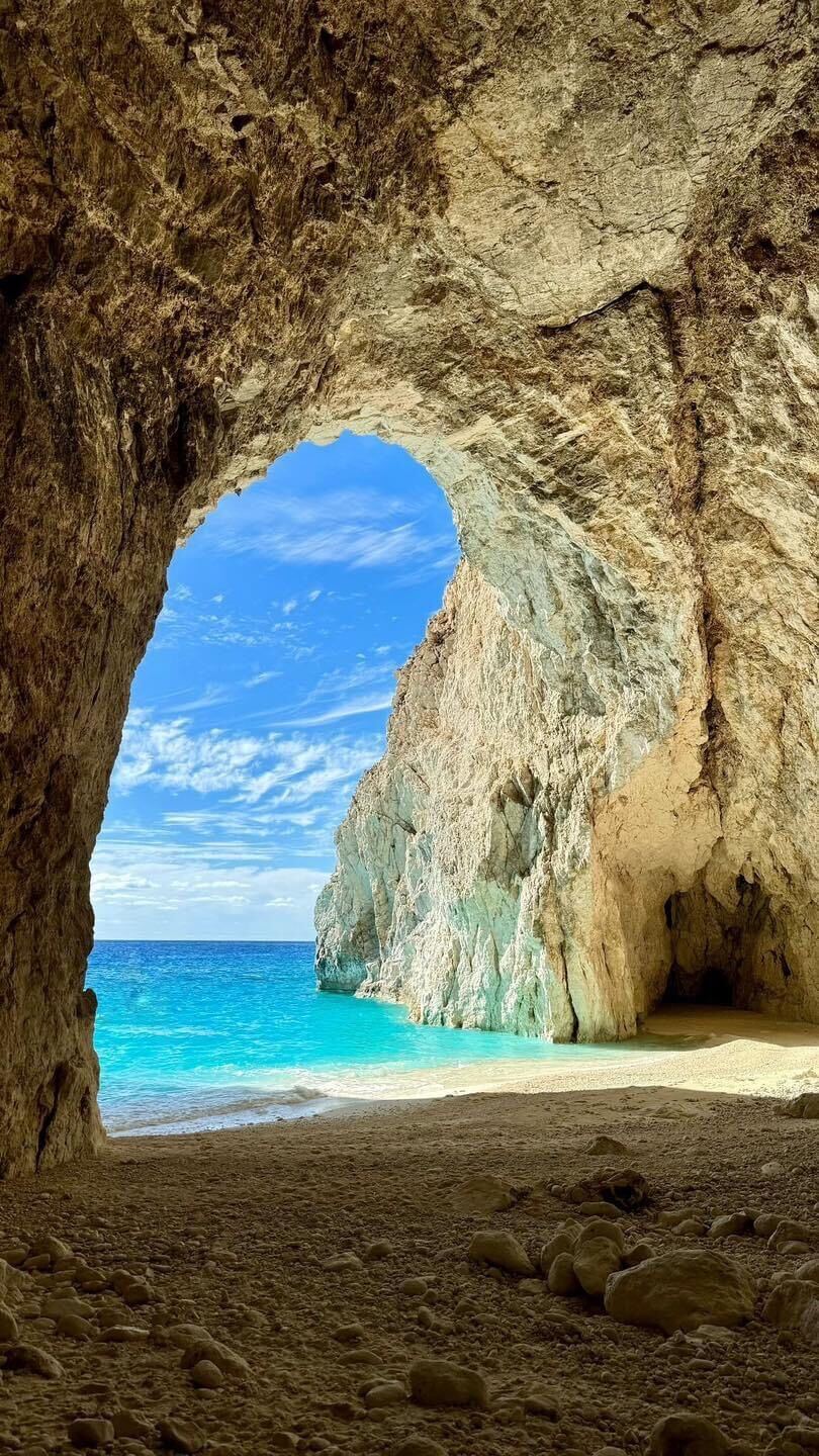 View from inside the cave looking out to the turquoise sea and blue sky through the towering rock arch
