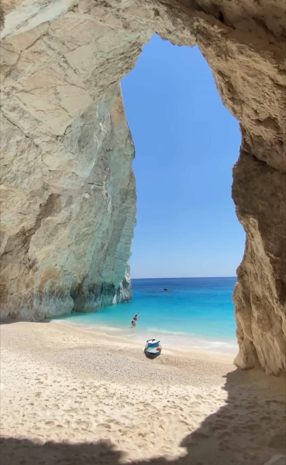 The heart-shaped cave opening with a person standing on the white sand beach below