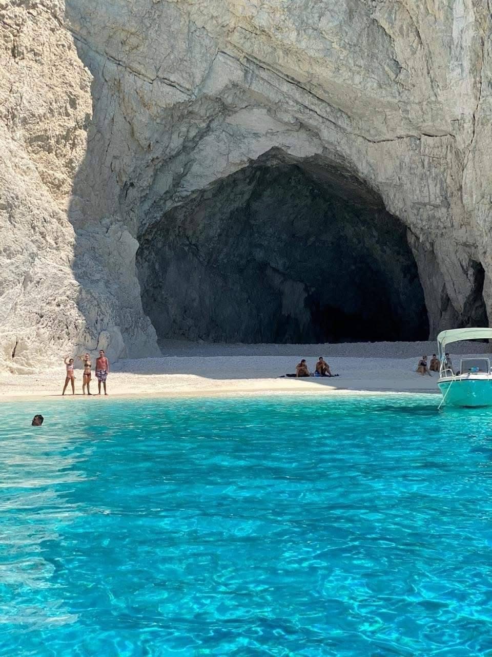 Cave entrance from the water with visitors on the sandy beach and turquoise shallows