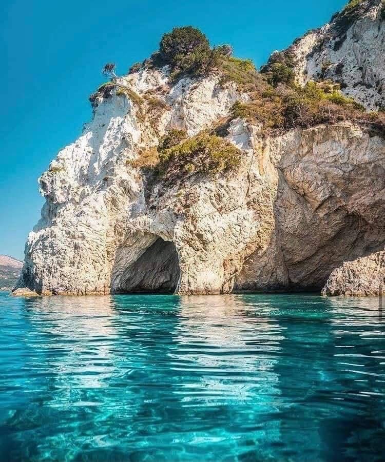 Dramatic cliff face with cave openings and lush vegetation above the turquoise sea