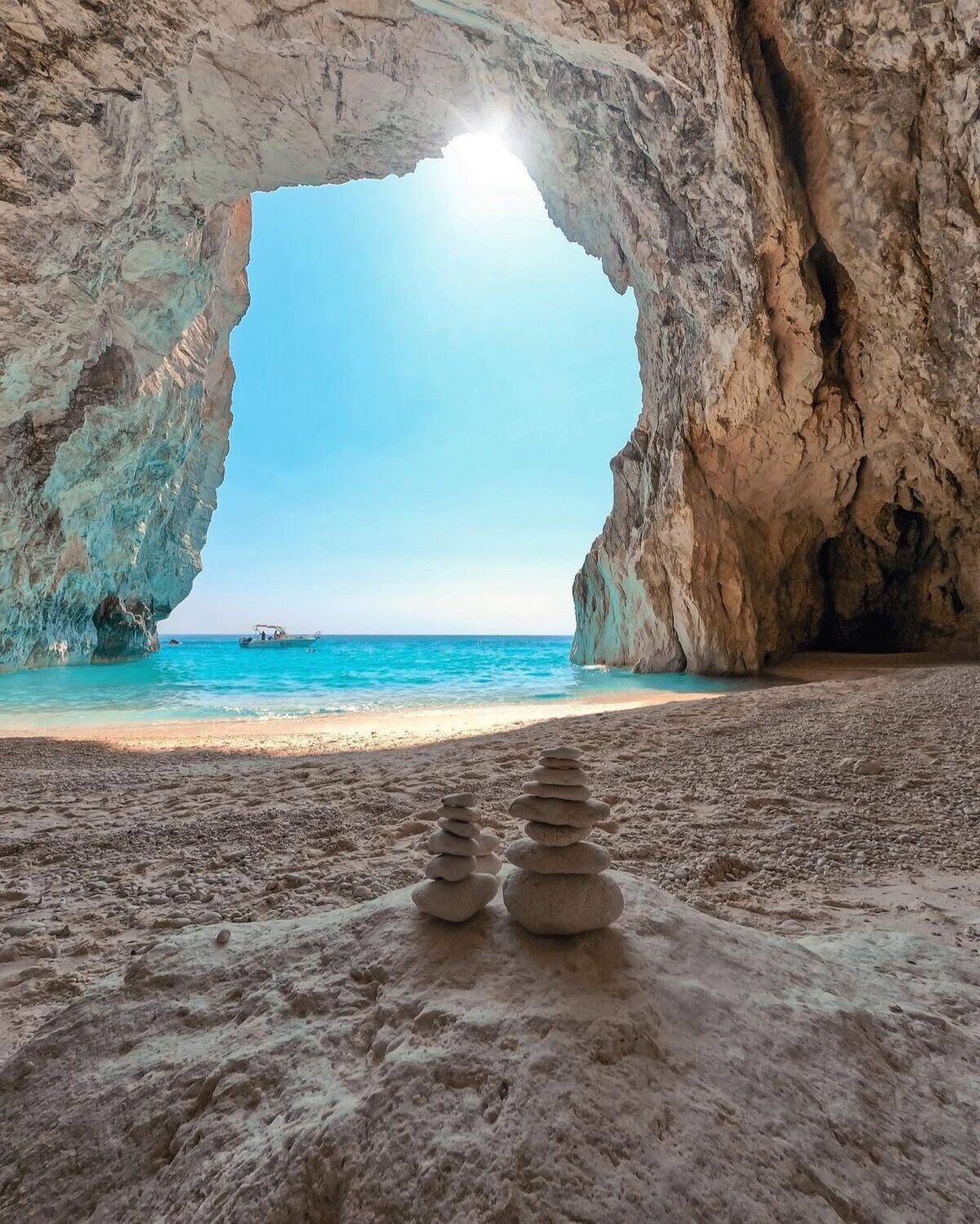 Inside Eros Cave with stacked zen stones on the sandy floor and the arch framing the sea
