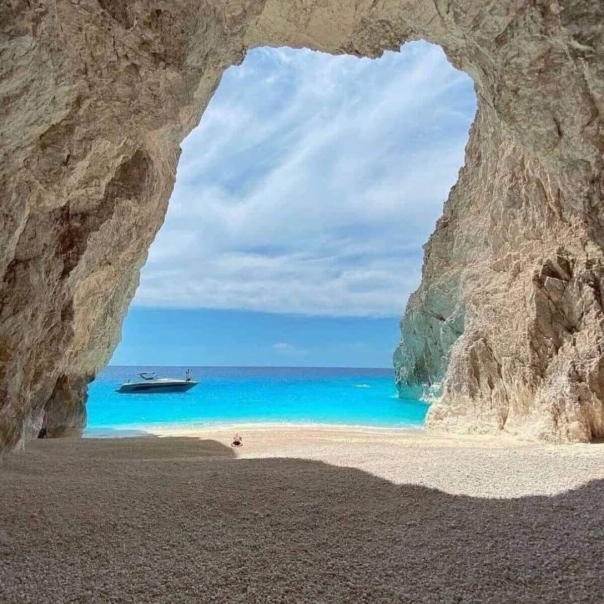 View from inside Eros Cave looking out through the arch to the turquoise sea and a boat