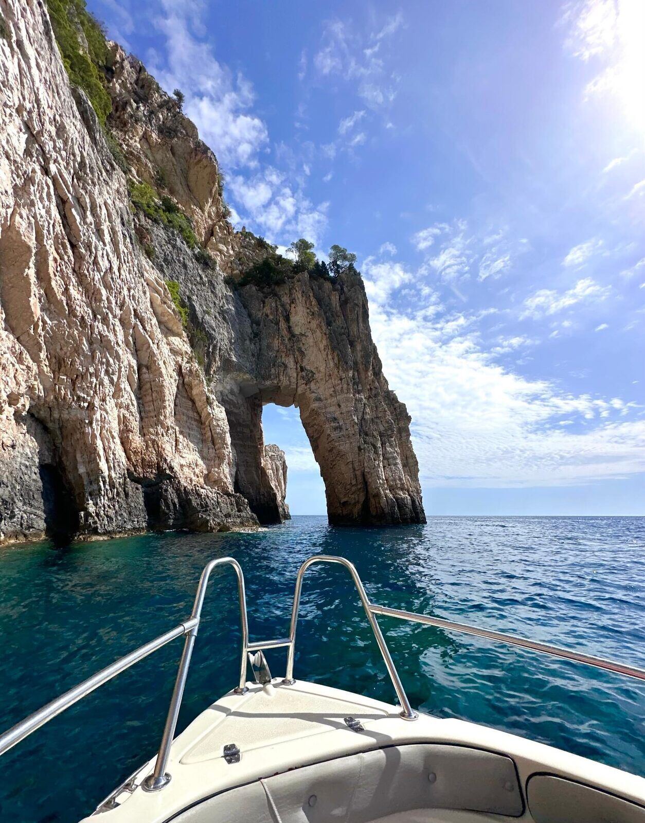 View from the bow of a speed boat approaching the iconic Keri sea arch with sunlight behind