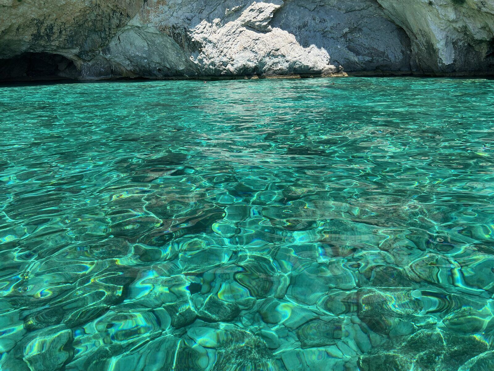 Sunlight filtering into a sea cave onto bright turquoise water at the Keri Caves