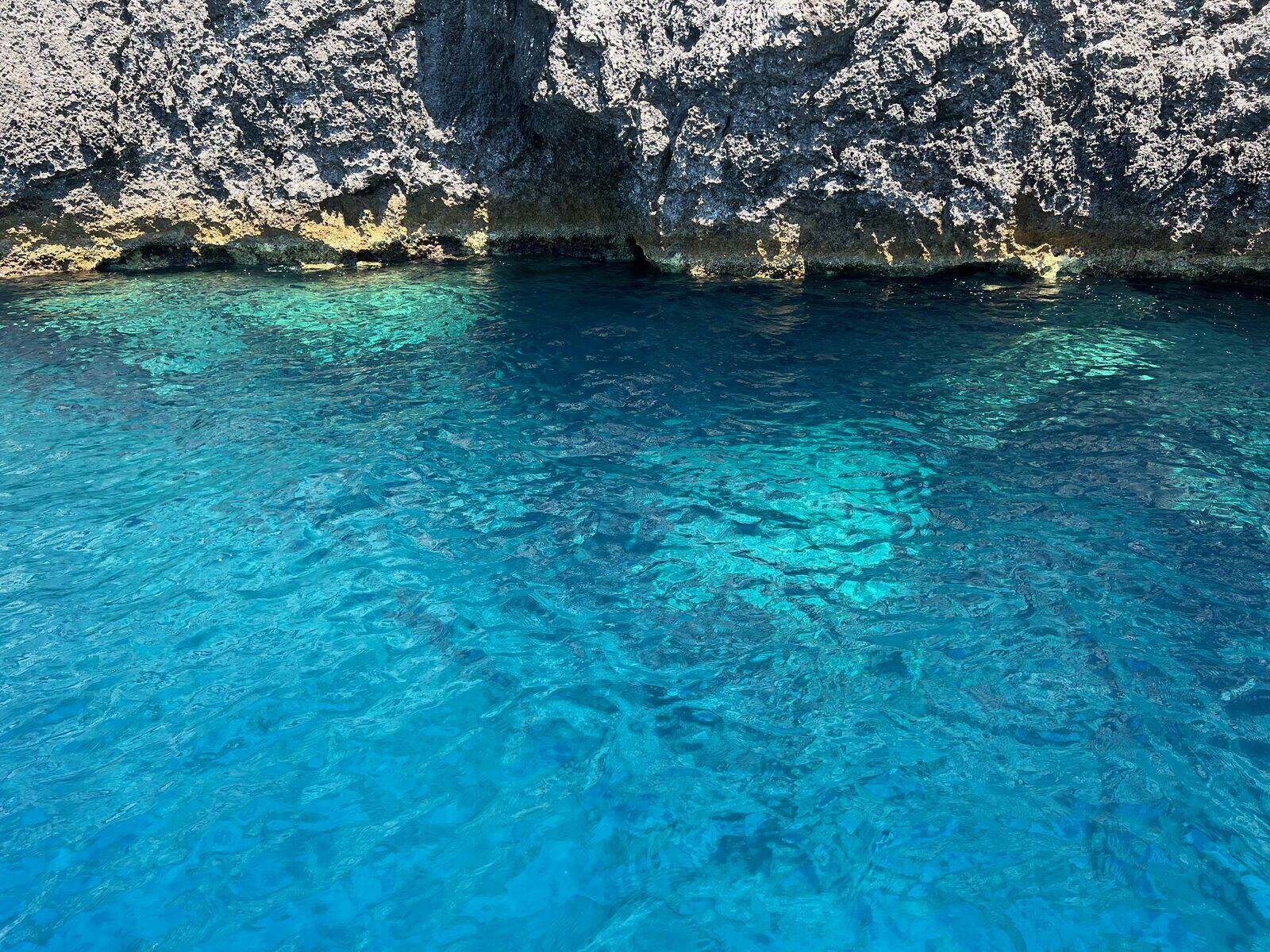 Crystal-clear turquoise water beneath the rocky shoreline at the Keri Caves
