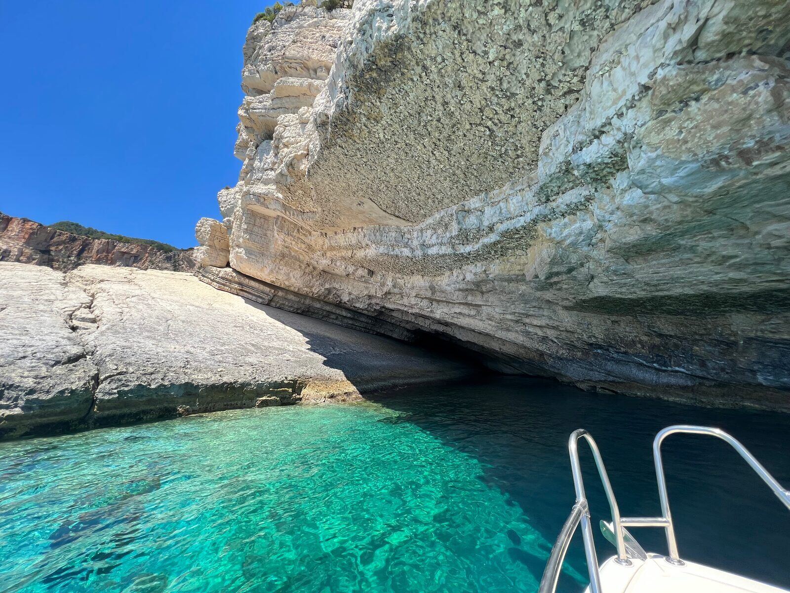 Undercut limestone cliff overhanging the turquoise water beside the boat