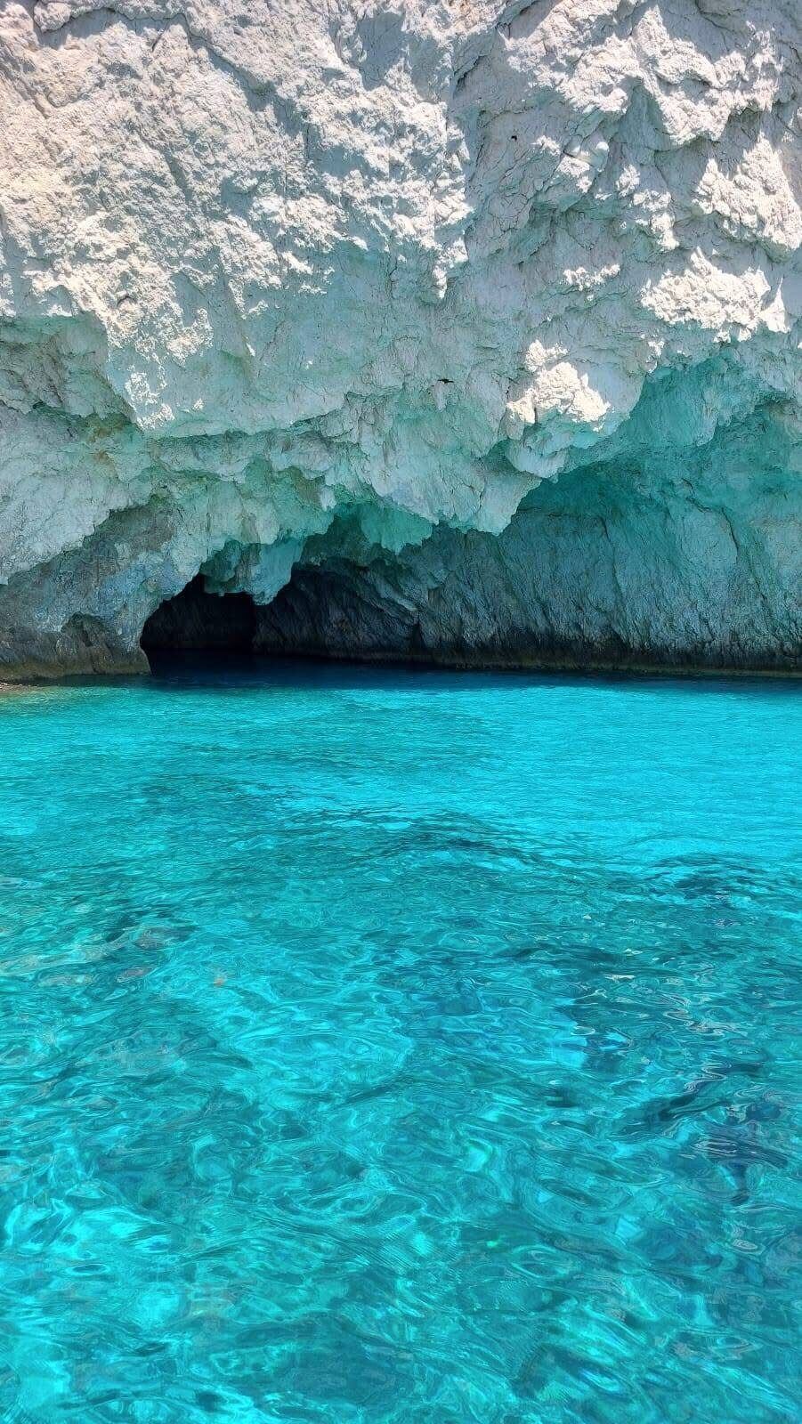 Cave entrance carved into the cliff above vivid turquoise water at the Keri Caves