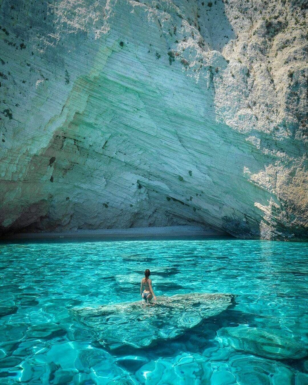 Swimmer on a submerged rock dwarfed by the immense white limestone cliff behind
