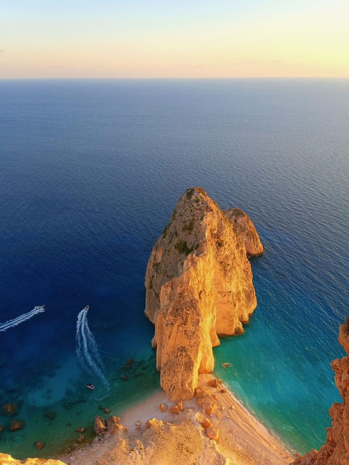 Myzithres rock bathed in golden hour light with a boat wake below