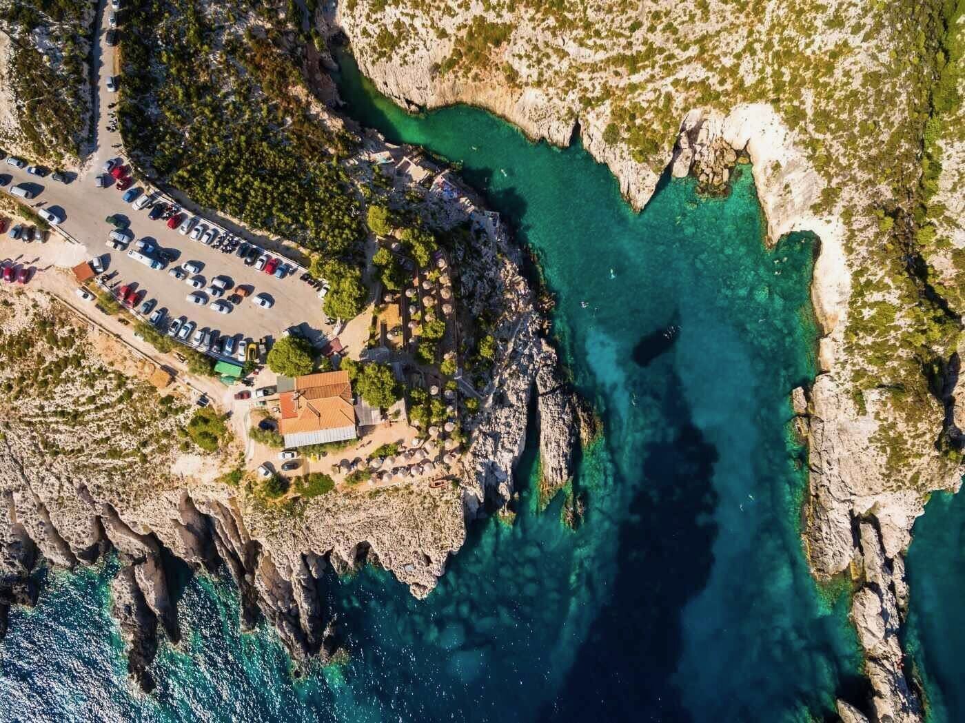 Overhead aerial of Porto Limnionas with the taverna, parking and turquoise water carved into white limestone cliffs
