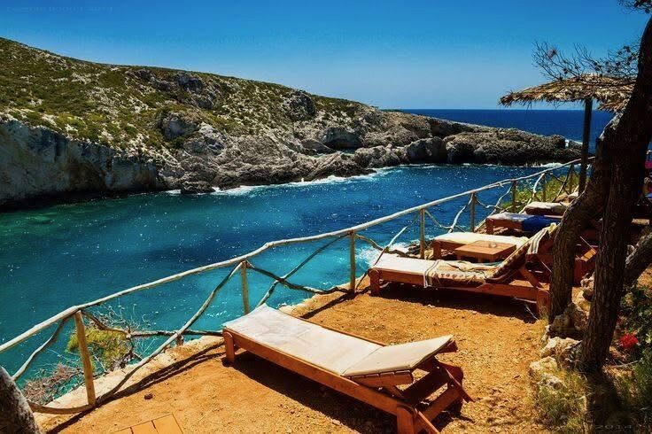 Wooden sun loungers on a platform with railings overlooking Porto Limnionas bay
