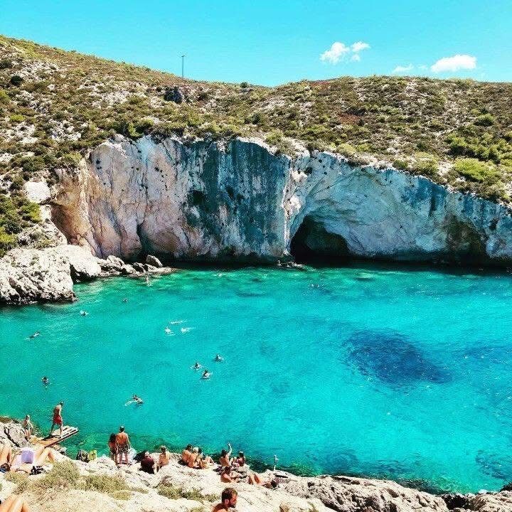 Wide view of Porto Limnionas with swimmers in the bay below an overhanging white limestone cliff