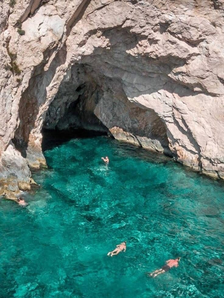 Swimmers floating in the turquoise water inside a sea cave at Porto Limnionas