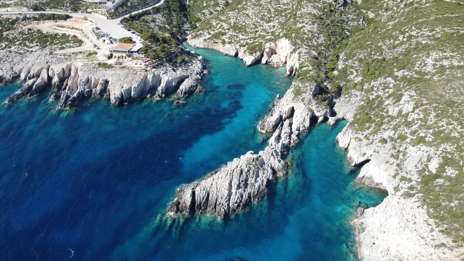 Aerial view of the Porto Limnionas inlet with turquoise water, white limestone cliffs and the clifftop taverna