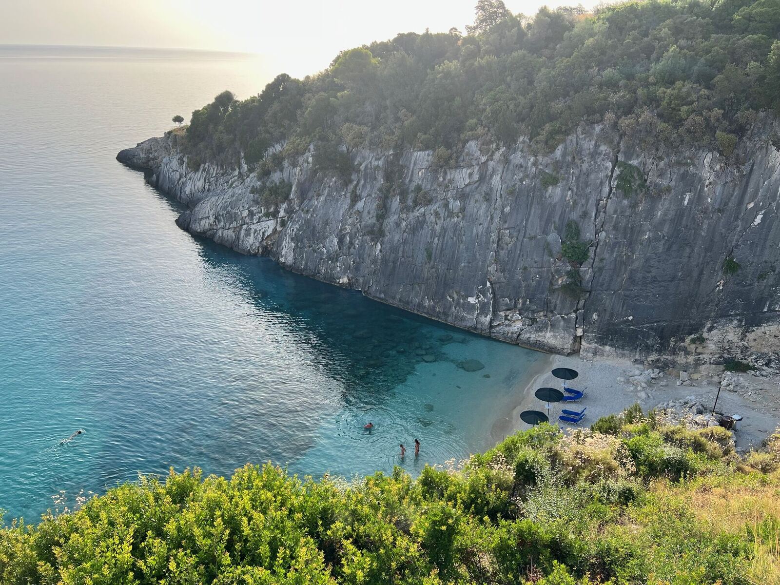 Golden hour view of Xigia Beach with towering limestone cliff and crystal-clear water