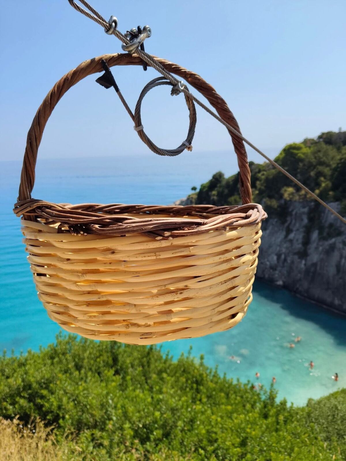 Traditional wicker basket on a zipline with the Xigia cove in the background