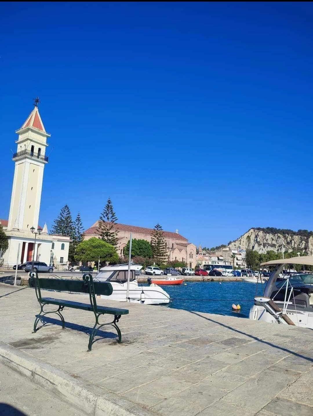 Harbour promenade with bench, bell tower, and moored boats