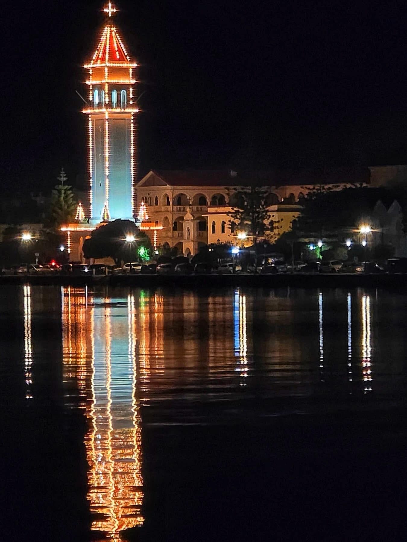 Church bell tower lit up at night with warm reflections on the harbour